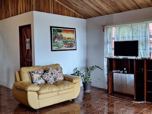 A living room with a sofa, a TV on a stand, a painting on the wall, and a door with a sign.
