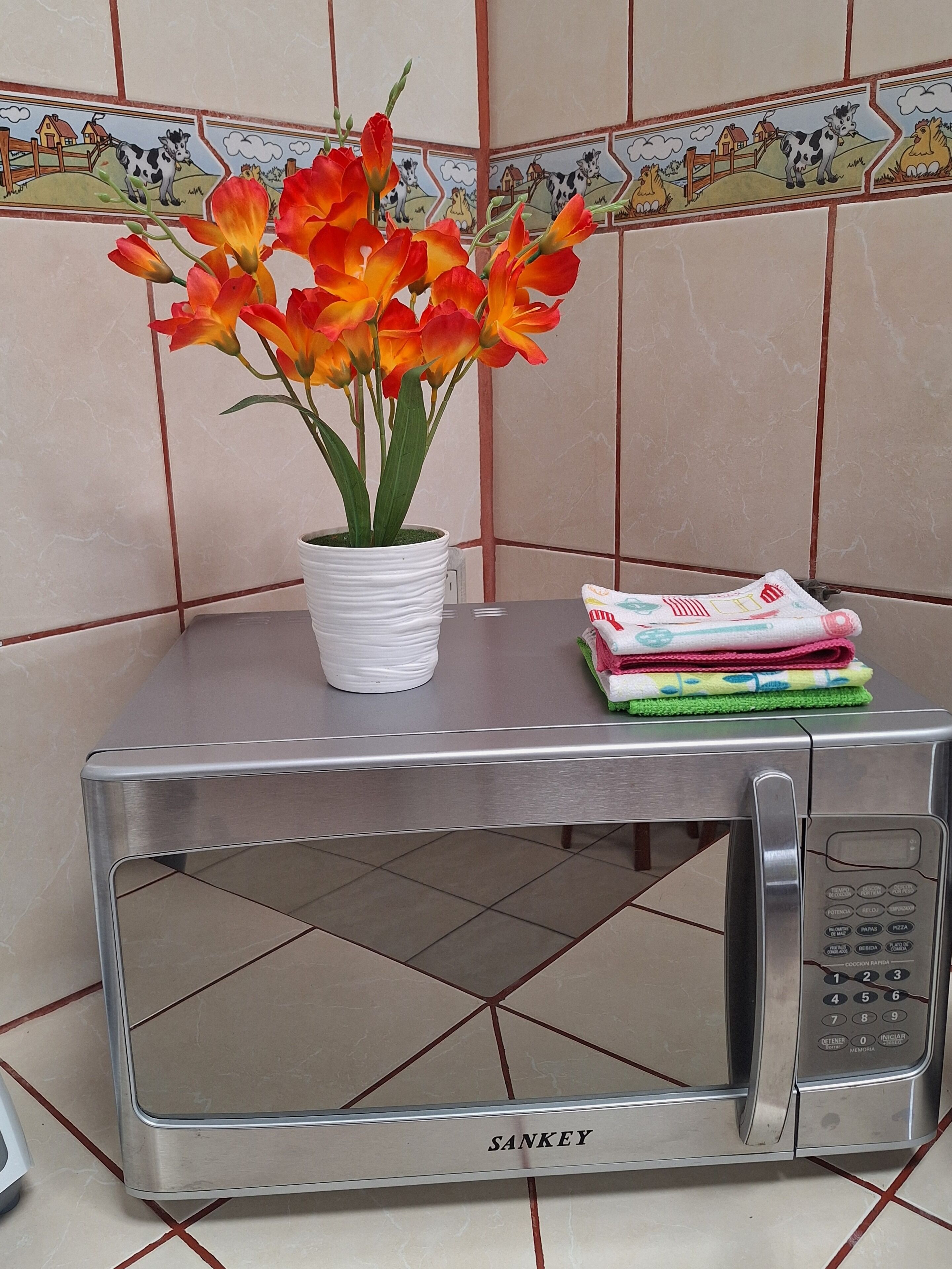 Eine Mikrowelle aus Edelstahl mit einem weißen Topf, der mit orangefarbenen Blumen bepflanzt ist.