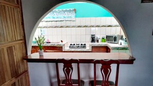 A kitchen with a tiled backsplash, a stove, a microwave, and a sink. There are two wooden chairs in front of a bar counter. - Bosque del Río Lodging (Monteverde)