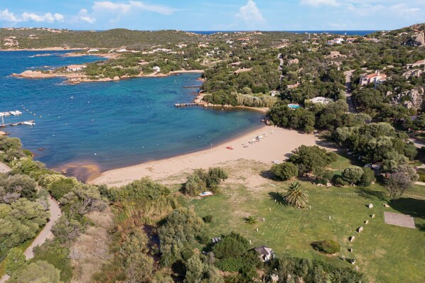 An aerial view of a coastal area with a beach, boats, and scattered houses.