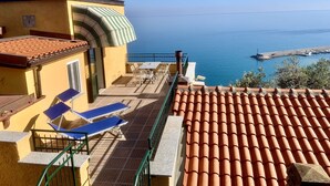 A balcony with a table and chairs, overlooking a coastal area with a clear view of the sea and a small pier. - Beautiful panoramic terrace overlooking the sea, with swimming pool (Finale Ligure)