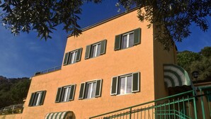 A multi-story building with a yellow facade, green shutters, and a stone base. - Beautiful panoramic terrace overlooking the sea, with swimming pool (Finale Ligure)