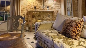A cozy room with a stone wall, a wooden ceiling, a sofa with patterned upholstery, a small table with lamps, and a chair. - Manor of Quintefeuille /Tennis -exceptional estate for 12 people max (Journiac)