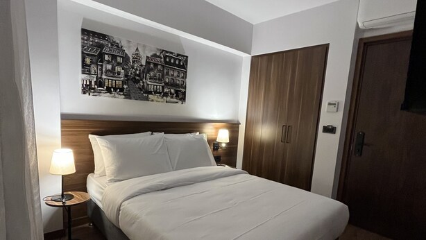 A neatly arranged bedroom with a bed, bedside lamps, a wall-mounted artwork, a wardrobe, and a door. - PALMERA HAGIA SOPHIA (Istanbul)