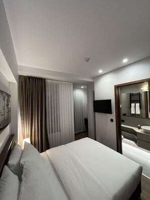 A hotel room with a bed, a bedside table, a TV, a bathroom with a sink, and a mirror. - PALMERA HAGIA SOPHIA (Istanbul)