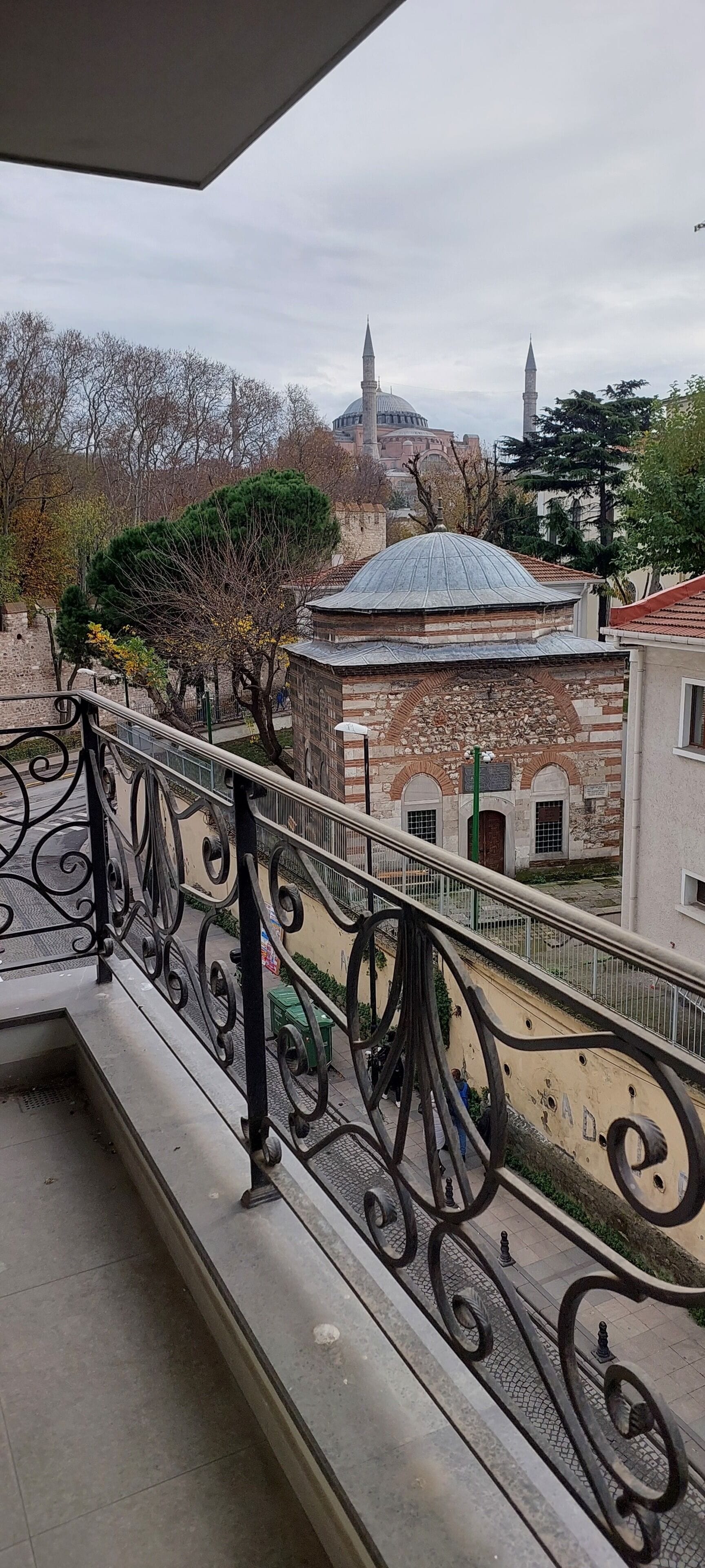 Un balcón con barandillas metálicas ornamentadas que da a un edificio histórico con una cúpula y un minarete.
