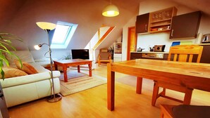 Avoin, loft-tyylinen olohuone, jossa on ruokailutila, sohva, puinen pöytä ja portaikko.