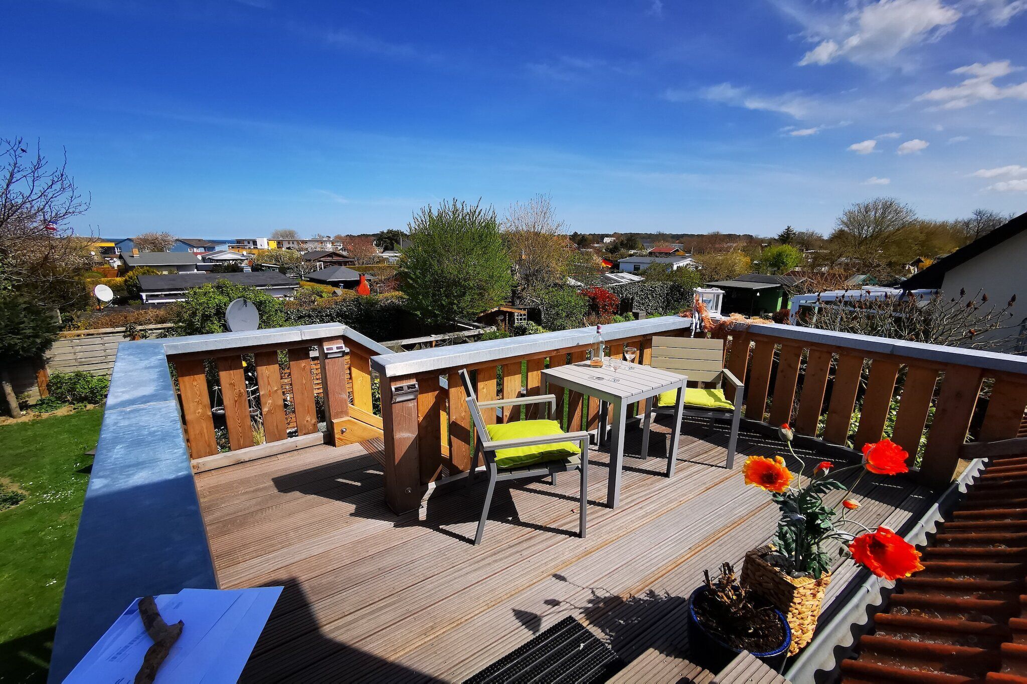 A deck with a table and chairs, surrounded by a wooden railing, overlooking a residential area.