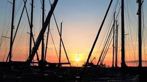 Satamassa oli useita purjeveneitä, taivas oli kirkas ja aurinko laski horisonttiin.