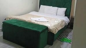 A bedroom with a green upholstered bed, a matching green ottoman, white bedding, and beige curtains. - A spacious & lovely 1 bedroom homestay in Nakuru (Nakuru)