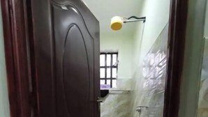 A narrow hallway with a dark wooden door, a tiled floor, and a pink mat leading to a bathroom with a white toilet and a shower area. - A spacious & lovely 1 bedroom homestay in Nakuru (Nakuru)