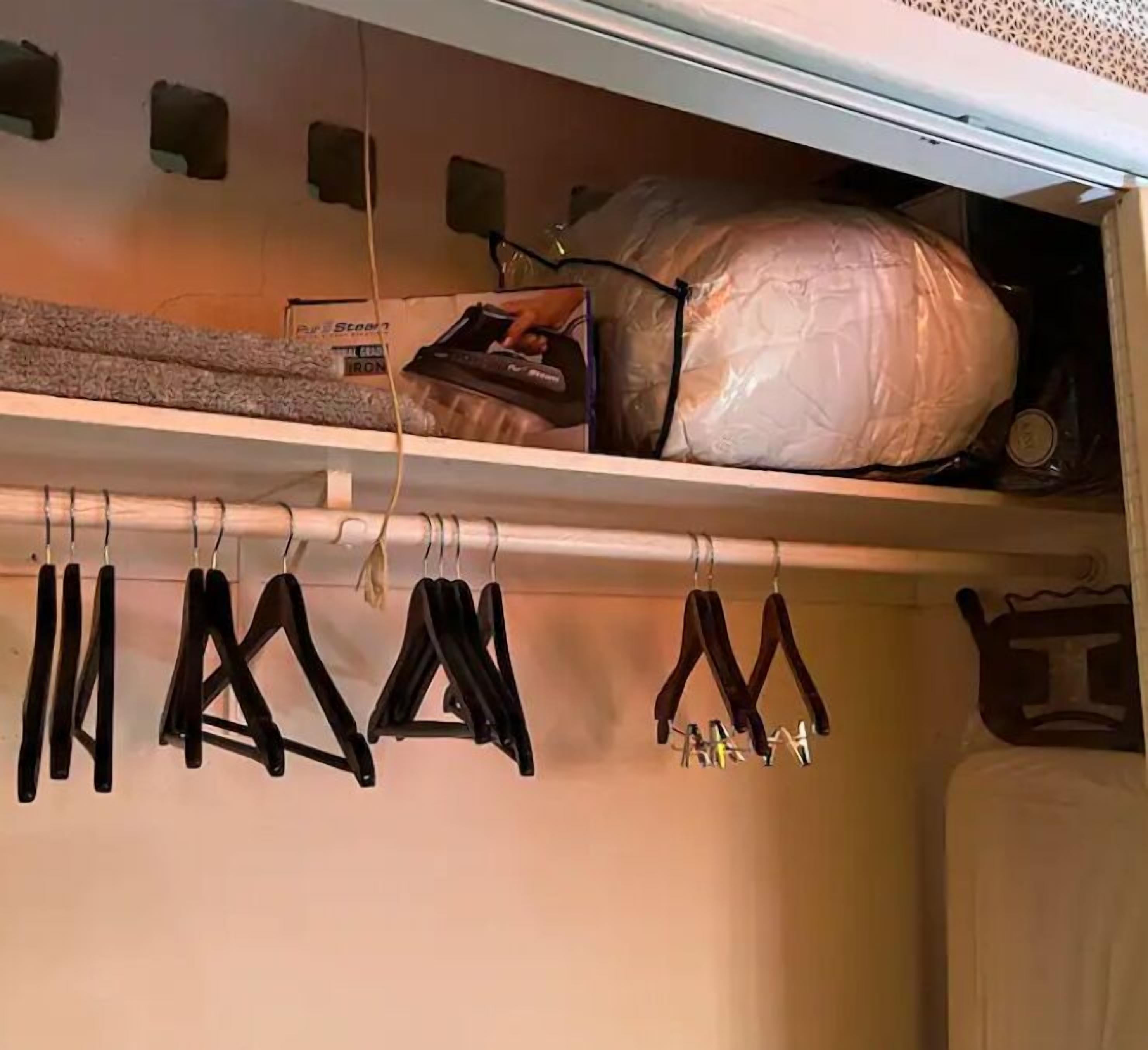 A closet with hanging clothes and a shelf with a bag and a box.