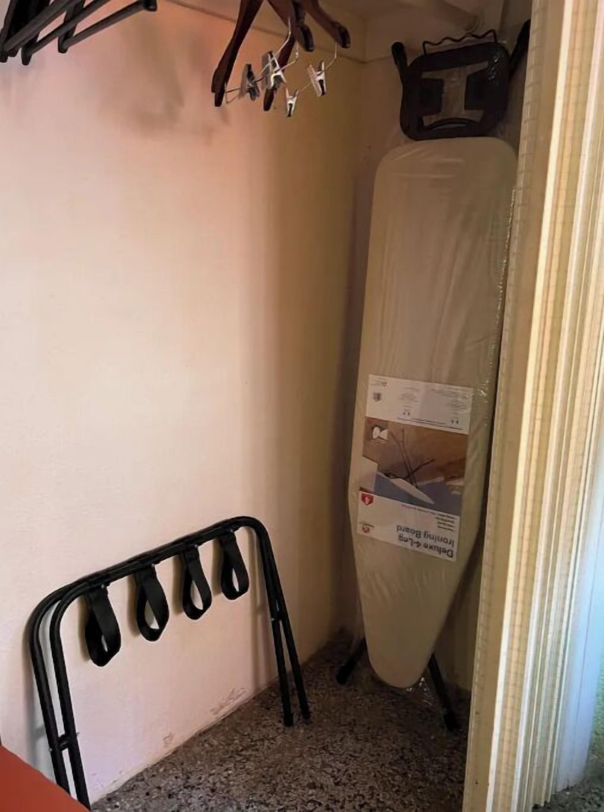 Een hoek van een kamer met een zwarte metalen stoel, een matras op een standaard en een wandrek met kledinghangers.