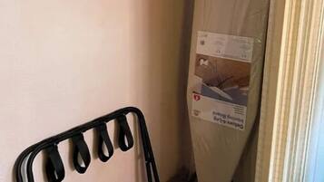 Een hoek van een kamer met een zwarte metalen stoel, een matras op een standaard en een wandrek met kledinghangers.