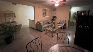 Un salon comprenant un canapé, deux fauteuils, une table basse, un ventilateur de plafond et un réfrigérateur.