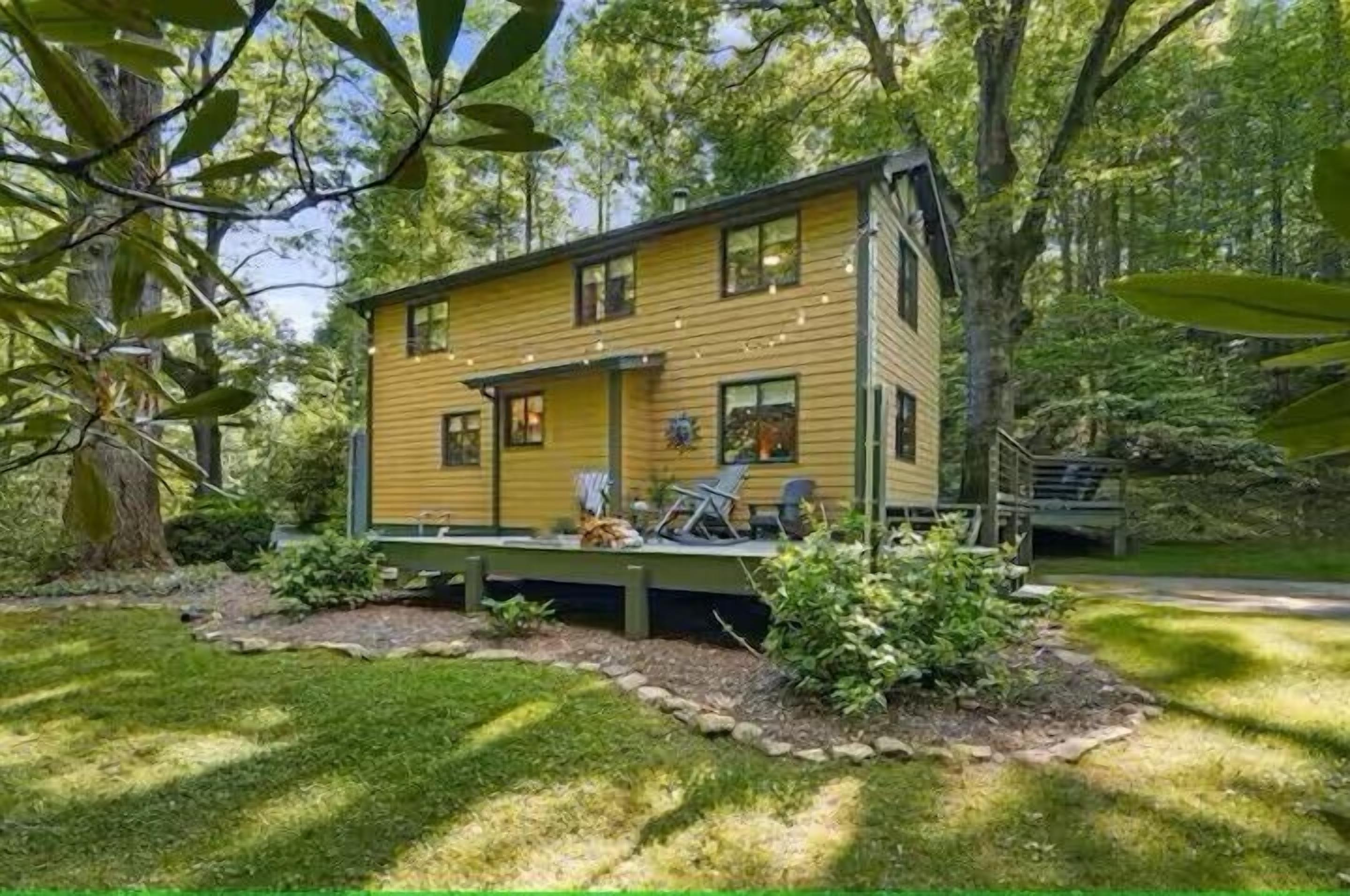 A wooden cabin with a deck, surrounded by trees and a well-maintained lawn.