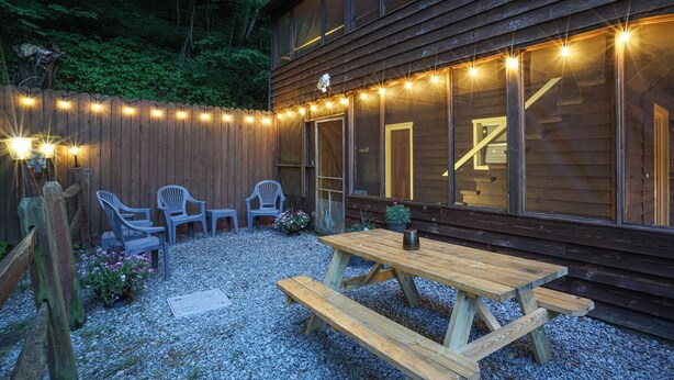 A wooden deck with a picnic table and chairs, surrounded by a wooden fence and string lights. - Secluded Lodge w/ grill + Free Coffee and Tea (Elkins)