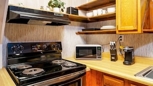 A compact kitchen with a black stove, a microwave, wooden shelves, and a coffee maker. - Secluded Lodge*Full kitchen + King Bed (Elkins)