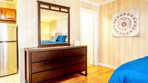A bedroom with a wooden dresser, a mirror, a bed with blue bedding, a wall art piece, and a wooden floor. - Secluded Lodge*Full kitchen + King Bed (Elkins)