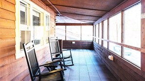 A covered porch with wooden walls and large windows, featuring a bench and chairs. - Secluded Lodge*Full kitchen + King Bed (Elkins)