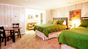 A hotel room with two beds, a wooden headboard, a small table with chairs, a vanity with a mirror, and a painting on the wall. - Secluded Lodge w/ grill + Free Coffee and Tea (Elkins)