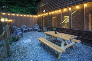 A wooden deck with a picnic table and chairs, surrounded by a wooden fence and string lights. - Secluded Lodge w/ grill + Free Coffee and Tea (Elkins)