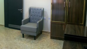 A room with a dark wooden wardrobe, a grey upholstered armchair, and a tiled floor.