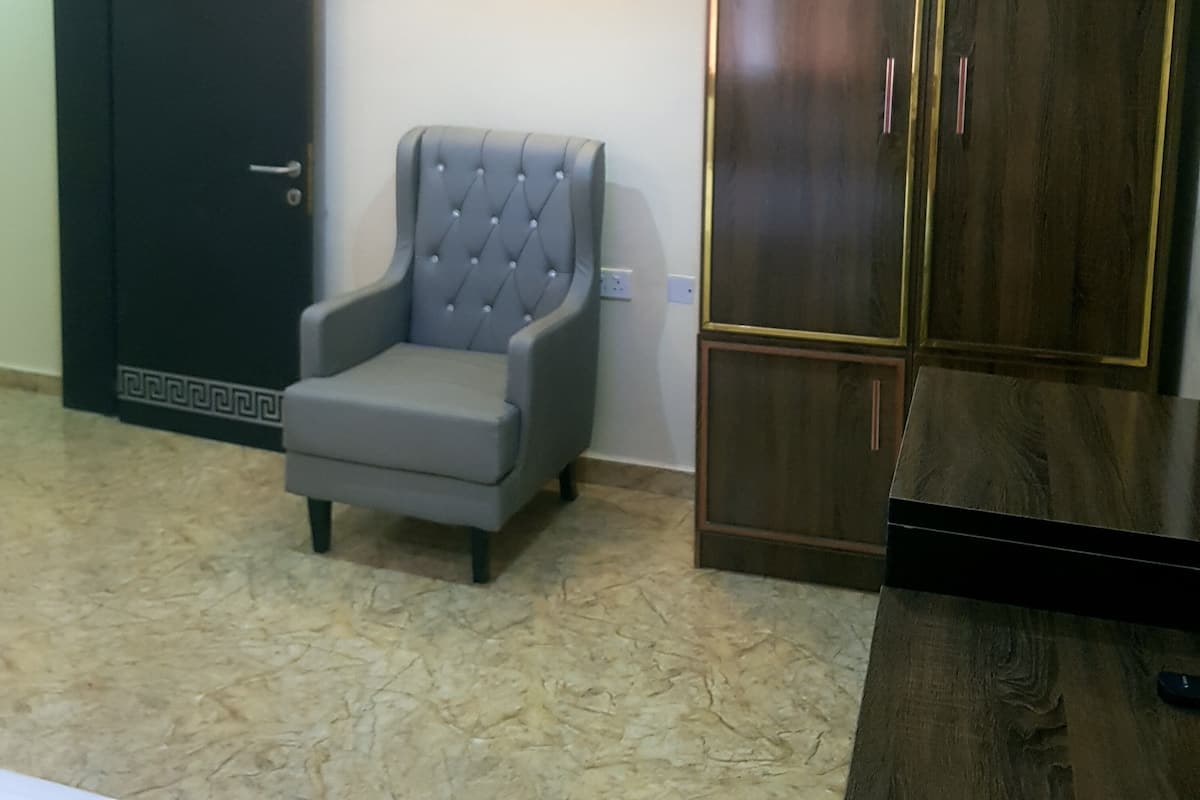 A room with a dark wooden wardrobe, a grey upholstered armchair, and a tiled floor.