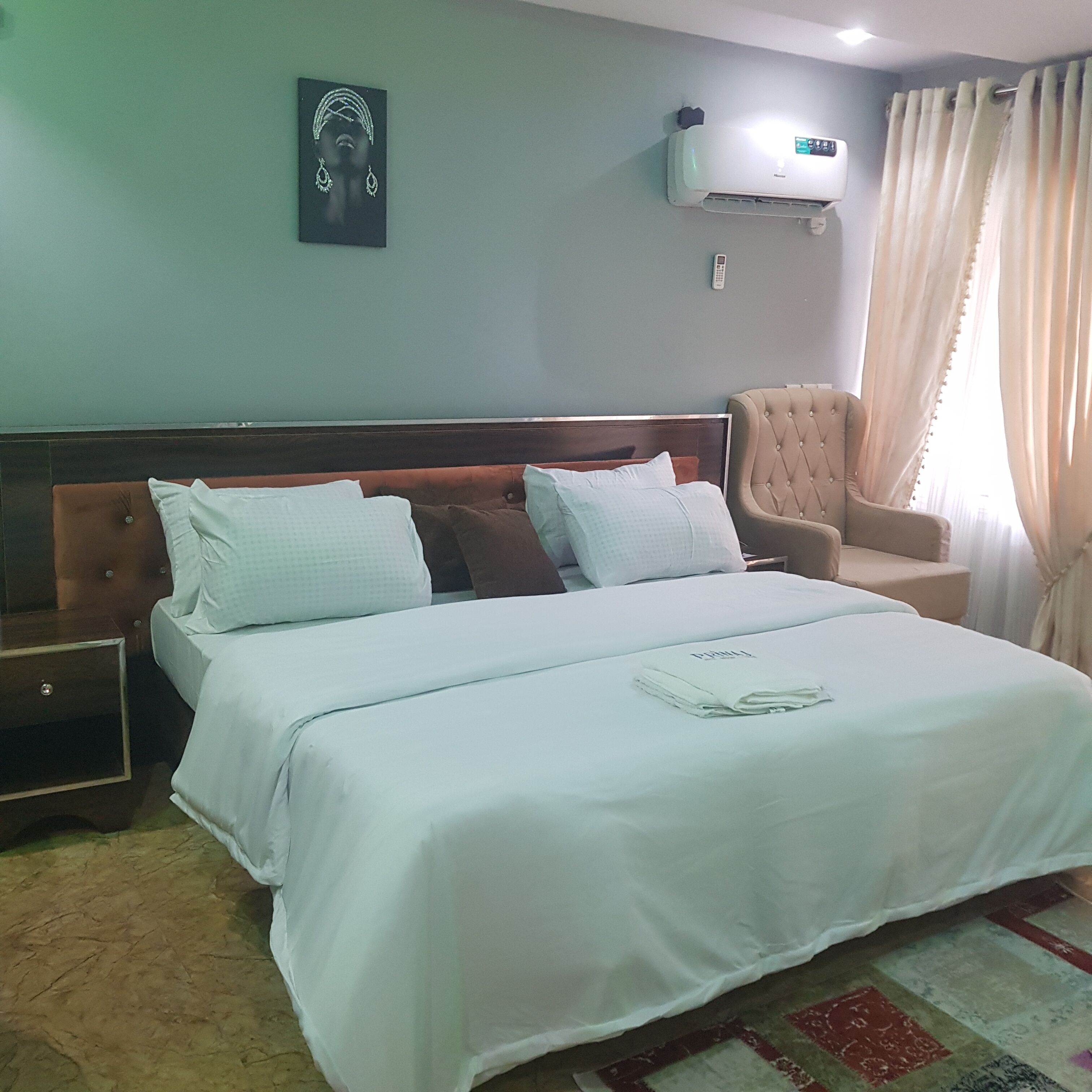 Une chambre d’hôtel avec un grand lit, une table de chevet, une chaise et un climatiseur fixé au mur.