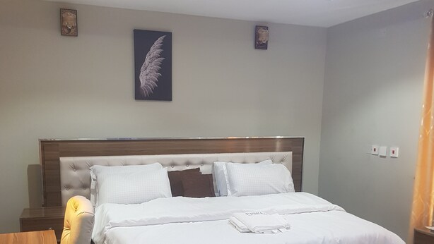 A neatly made bed with white linens, a wooden headboard, and a decorative feather wall hanging.