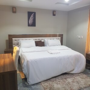 Un lit bien fait, avec du linge de lit blanc, une tête de lit en bois et une décoration murale en plumes.