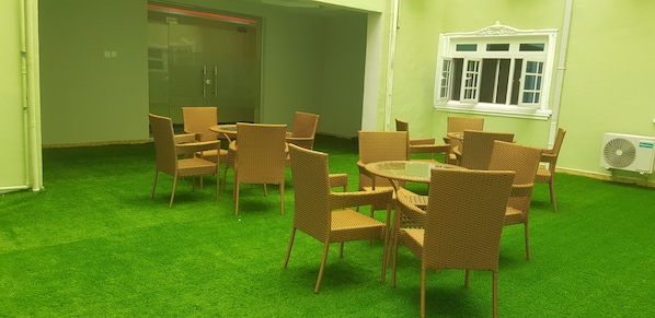 A room with green artificial grass, wicker furniture, a glass door, and a window with white trim.