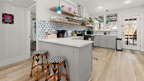Une cuisine moderne dotée d’un îlot central, de tabourets de bar, d’étagères en bois et d’un crédence décorée.