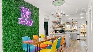 Une cuisine moderne avec des meubles blancs, un îlot central en bois et un néon fixé sur un mur vert.