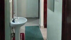 Ein Flur mit einem weißen Waschbecken, einem grünen Teppich und einer Tür rechts.