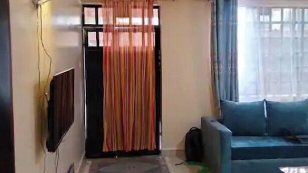 Ein Wohnzimmer mit einer Couch, einem an der Wand montierten Fernseher und einem Vorhang.