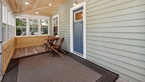 A covered porch with a wooden ceiling, a table with chairs, and a blue door.