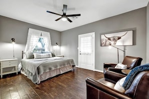 A bedroom with a bed, bedside tables, a ceiling fan, a chair, and a wall-mounted TV.