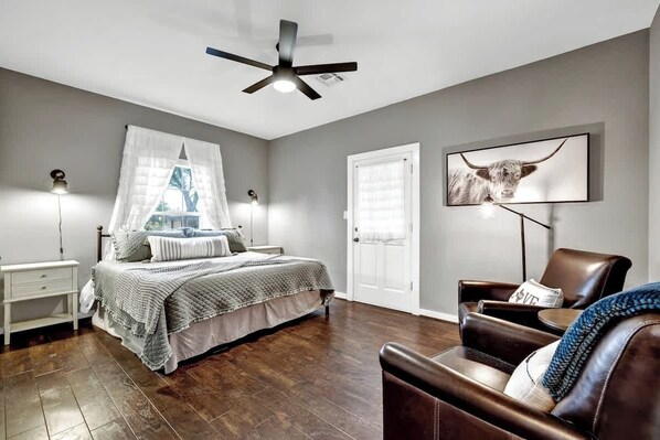 A bedroom with a bed, bedside tables, a ceiling fan, a chair, and a wall-mounted TV.