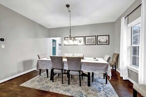 A dining room with a table set for four, a chandelier, and framed artwork on the wall. - The Country Haus: Quaint home 1 mile from Downtown (Fredericksburg)