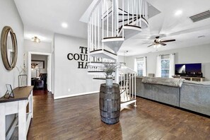 A modern living room with a spiral staircase, a grey sofa, and a large mirror on the wall. - The Country Haus: Quaint home 1 mile from Downtown (Fredericksburg)