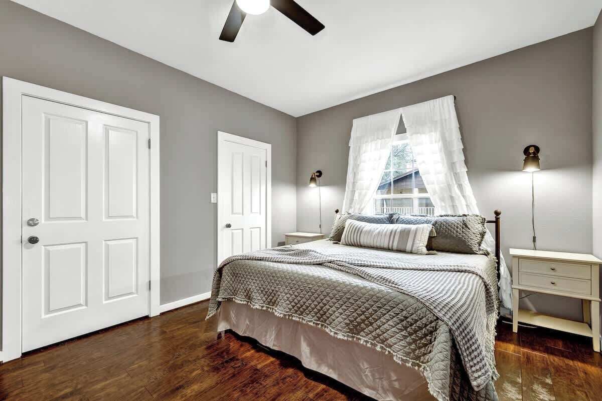 Une chambre à coucher avec un lit, des tables de chevet, un ventilateur de plafond et une fenêtre avec un rideau blanc.