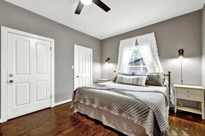 A bedroom with a bed, bedside tables, a ceiling fan, and a window with a white curtain. - The Country Haus: Quaint home 1 mile from Downtown (Fredericksburg)