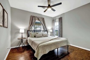 A bedroom with a bed, a standing lamp, a ceiling fan, and a window with curtains.
