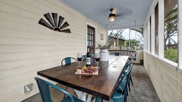 A covered patio with a wooden table set for dining, featuring a bottle of wine, glasses, and a fruit platter.