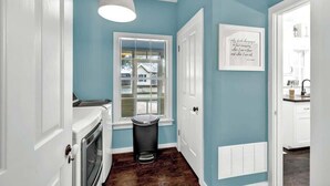 A hallway with a white door, a window with a view, a trash can, and a wall-mounted vent.