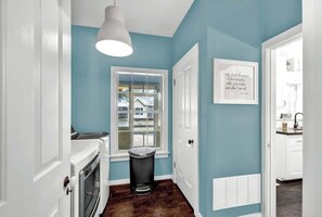 A hallway with a white door, a window with a view, a trash can, and a wall-mounted vent.