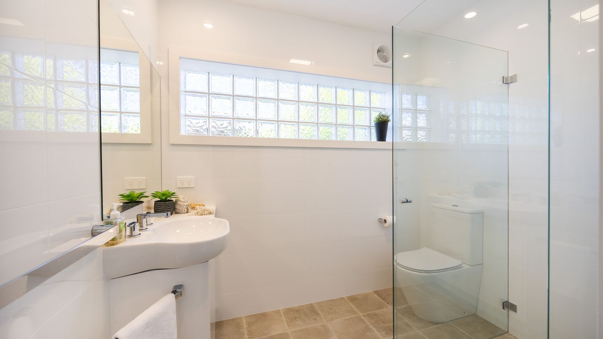 A modern bathroom with a glass shower enclosure, a white sink with a mirror, and a window above the sink.
