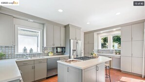 Une cuisine moderne avec des meubles gris, un îlot central, un four à micro-ondes encastré et un réfrigérateur.