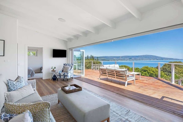 A spacious living area with a large window overlooking a scenic view, a cozy seating area with a wooden deck, and a flat-screen TV mounted on the wall.